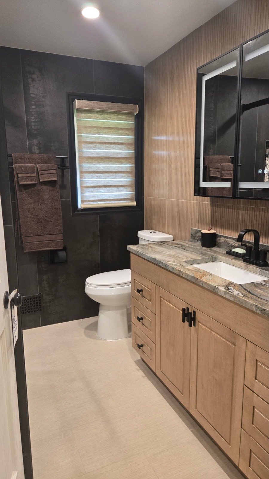 Renovated bathroom with dark tile, a backlit LED medicine cabinet, and matte black fixtures