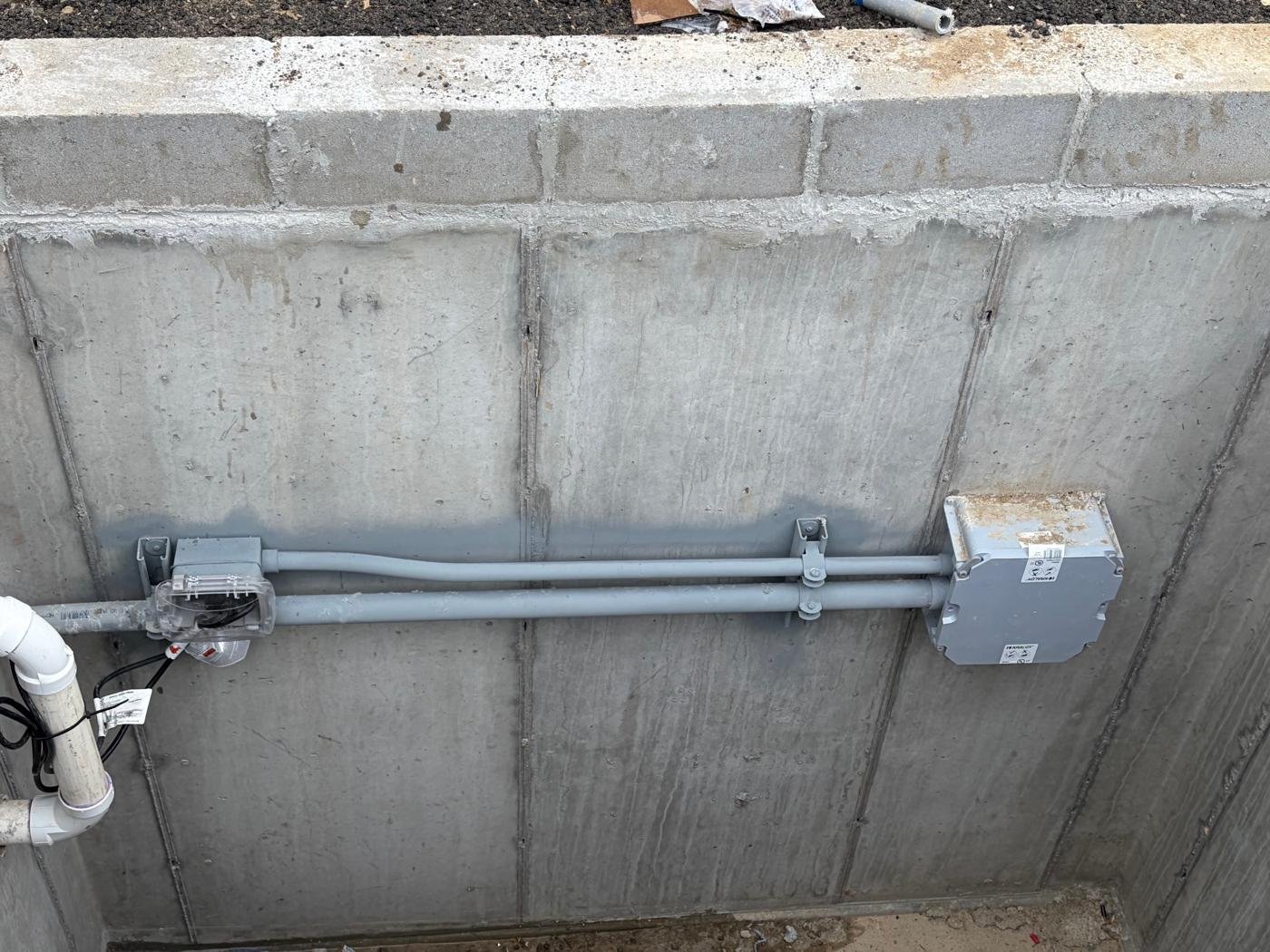 Conduit run and weatherproof junction box mounted on a poured concrete foundation wall