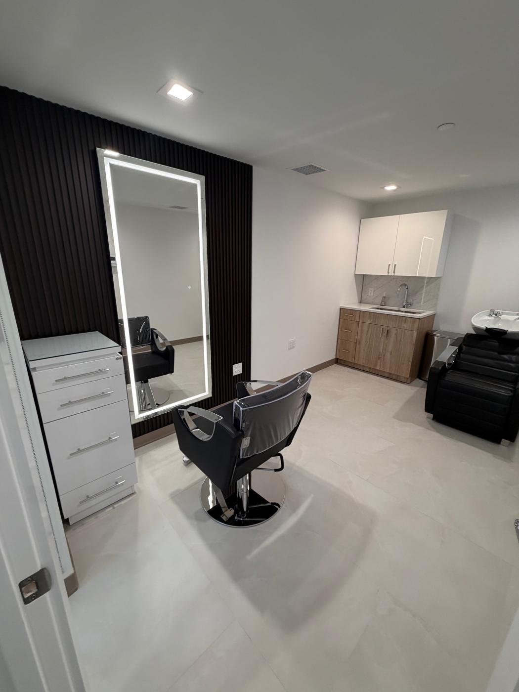 Full-length LED backlit mirror beside a dark slat accent wall in a salon